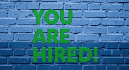 Obraz premium You Are Hired Green Text on Blue Brick Wall Background for Job Offer Announcement