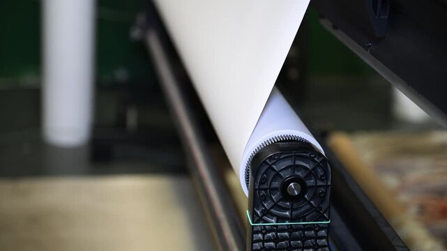 Feeding paper from a roll into a large format printer that prints advertising posters in the production room of the printing house