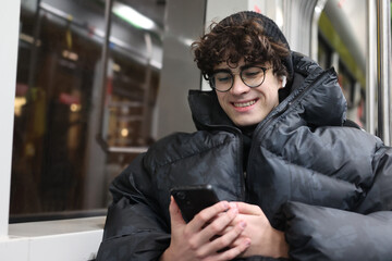 Obraz premium Smiling adolescent using mobile phone while commuting in the city. Modern youth lifestyle, daily commute, technology use, urban life and mobility concept.