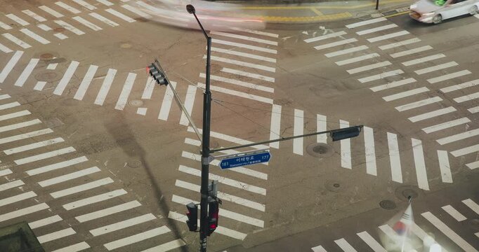 Aerial view of a bustling traffic intersection with vehicles navigating crosswalks and traffic lights transitioning between red and green. Time-lapse, Seoul, South Korea