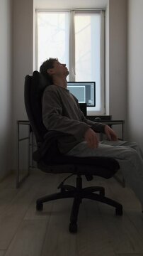 Young man wasting time in office chair instead of working, home office lifestyle during daytime, freelance routine, lack of motivation and modern work habits. . Vertical video