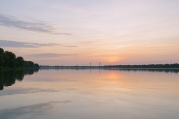 Obraz premium Serene River Landscape at Sunrise with Calm Water and Reflections, Featuring a Tranquil and Peaceful Ambiance
