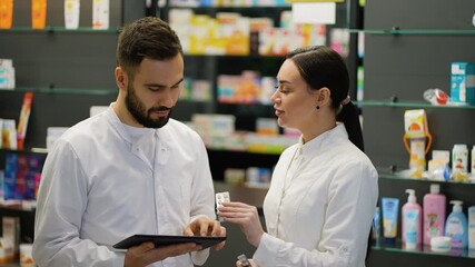 Two pharmacists talking and checking pills in pharmacy