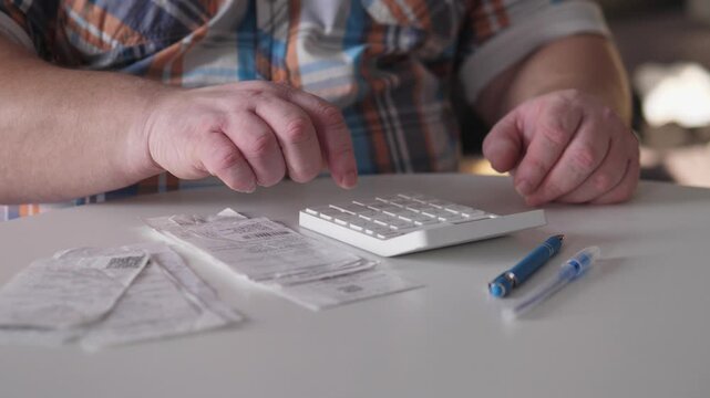 White Man Verifying Monthly Expenses With Calculator And Ledger On Table, Deliberate Pen Rests Beside Stacks Of Receipts, Neutral Indoor Light, Attentive Checking And Cross Referencing