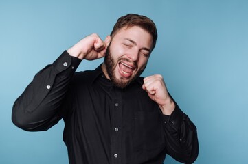 Man in black shirt dancing joyfully against blue background.