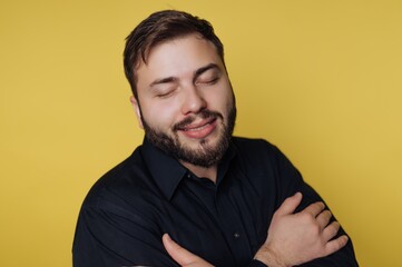Obraz premium Man in black shirt smiling with eyes closed against yellow background.