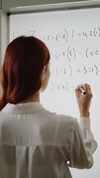 Redheaded mathematician writing complex algebraic equations on whiteboard. Academic research and problem solving in university setting. Vertical video with subtle panning and tilting movement.
