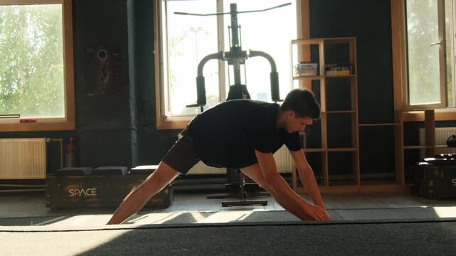 Man performs set of exercises stretching muscles against window. Athlete engages in workout session in gym with modern equipment slow motion