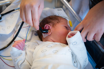Newborn baby receiving a hearing screening test by medical professional in a hospital, assessing...