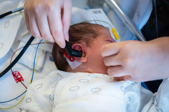 Newborn baby receiving a hearing screening test by medical professional in a hospital, assessing infant auditory health and developmental well-being at early age