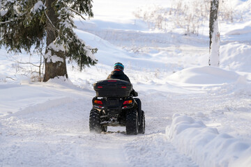 Individual riding an all-terrain vehicle on a snowy trail surrounded by trees in a winter landscape with fresh snow covering the ground © Natalia
