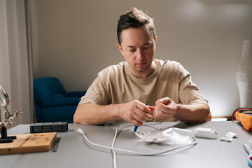 Man working with electronic components, stripping insulation from cable while repairing or assembling wiring, demonstrating hobby electronics project or household electrical maintenance.