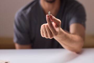 Person carefully holding pill amid scattered tablets and bottles, Individual attentively grasping...