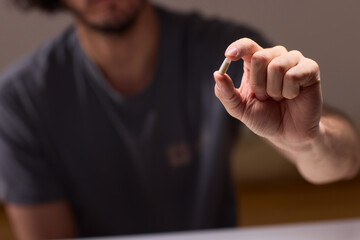 Person carefully holding pill amid scattered tablets and bottles, Individual attentively grasping...