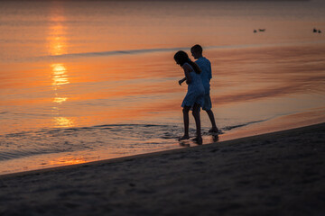 Siblings play around the beach enjoying waves and sun. Children walk along the beach at sunset holding hands. High quality photo