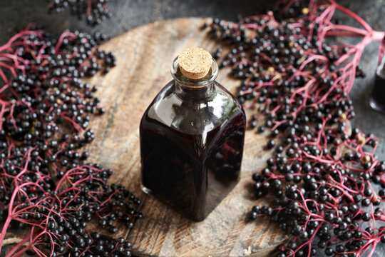 A bottle of black elder syrup with fresh elderberries