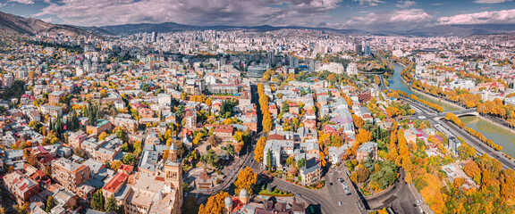 Aerial view over Tbilisi cityscape, showing the Mtkvari river winding through the urban area with autumn trees