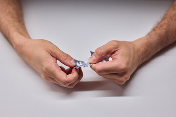 Hands extracting capsule from blister pack gently, closeup on fingertips and foil on white tabletop, quiet moment of dosing accuracy and calm preparation for intake