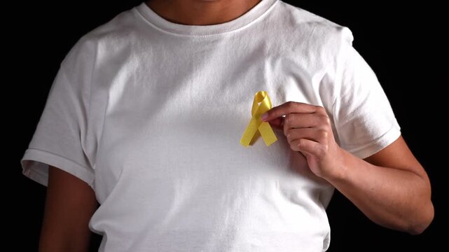 Anonymous woman holding a yellow ribbon in her hand and placing it on her chest. Awareness campaign for bladder cancer, sarcoma, and bone cancer