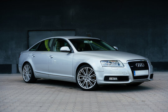A silver Audi A6 C6 Lift Quattro S Line parked facing forward against a dark building. German design with silver alloy wheels on an empty road. For marketing, advertising, or press releases.