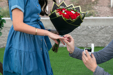 Man proposes to woman with diamond ring and red roses, she accepts