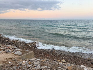 The sea reflects soft evening light under cloudy sky with distant horizon line. Calm waves, marine ecology and coastal landscape in seasonal outdoor environment.