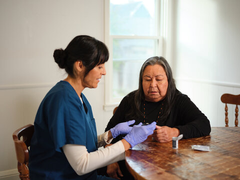 Native American elder woman has her glucose checked in dining room