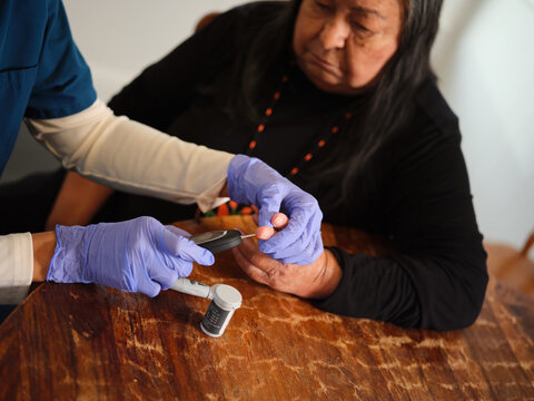 Native American nurse draws drop of blood from patient for glucose test