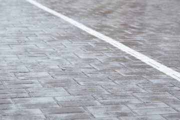 Wet cobblestone pavement covered with a thin layer of ice after freezing rain, with a white line marking the edge of the walkway in a city setting