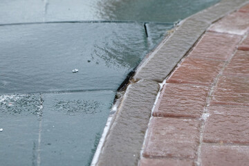 Ice-covered pavement showing a transition between gray concrete and red brick, with a thin layer of...