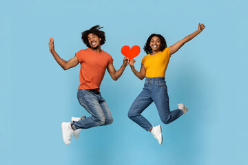 Happy african american young man and woman loving couple jumping up with heart-shaped red card over...