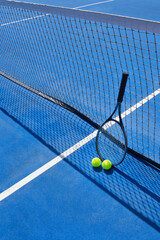 Tennis balls and a racket leaning against the net on a blue outdoor tennis court. © Ró & Photography