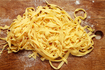 Texture of raw fresh egg pasta noodles scattered on wooden table. Uncooked homemade spaghetti background.