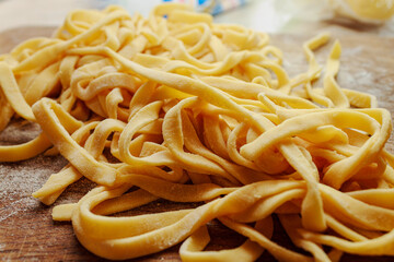 Pile of fresh homemade tagliatelle or fettuccine pasta noodles on wooden board. Raw italian food texture.