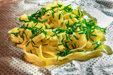 Homemade egg pasta with green onions served on aluminum foil tray. Rustic camping or takeaway food style.