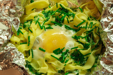 Baked pasta nest with egg yolk and green onions in foil. Hot cheesy noodle casserole dish.