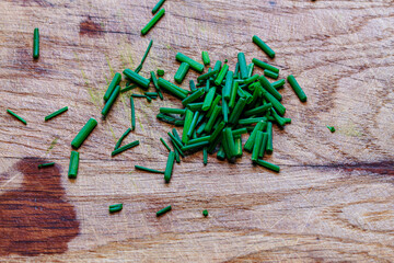 Fresh chopped green chives or spring onions scattered on rustic wooden board. Healthy herb ingredient.