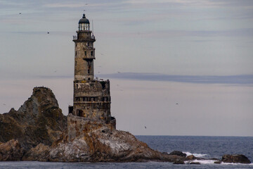 Old lighthouse stands tall against gloomy sky by the rocky shoreline with waves crashing nearby
