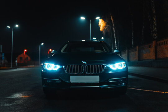 03.28.2023 - Kyiv, Ukraine. A BMW car with neon blue lights on is parked on the side of the road at night. M3 sports car with logo. Night city and drivers