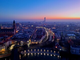 Obraz premium Aerial view of a modern European city at dusk with river, bridges and illuminated buildings during blue hour.