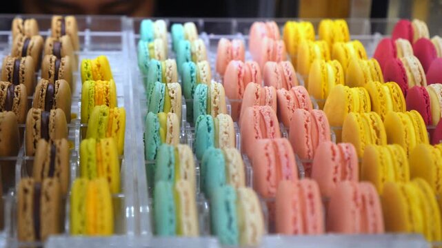 Rows of vibrant and delicious french macaron cookies sitting in a pastry shop display case, showing a variety of sweet flavors, colors, and fillings for sale in a bakery or gourmet food store