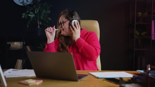 Funny female manager wearing headset, listening to music and singing at desk