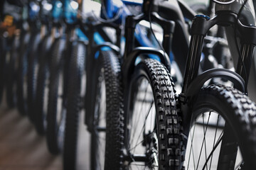 Close-up view of a row of new mountain bikes in a bicycle shop, focusing on tires and suspension.