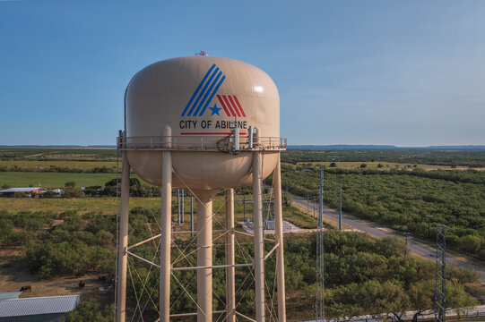 City of Abilene Logo on Brown Water Tower Surrounded Green Trees and Fields in Abilene, Texas Aerial Drone View