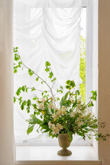 Elegant bouquet of white alstroemeria, peruvian lily flower in vintage bronze vase placed on window with white curtain in soft pastel interior background.