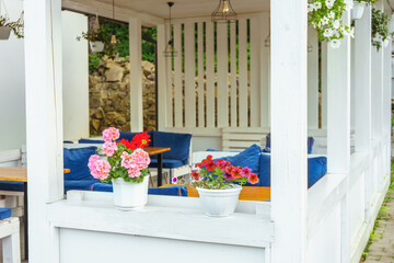 Cozy outdoor cafe, bistro or restaurant terrace exterior decorated with blooming flowers in pots. Summer restaurant seating, relaxing atmosphere, urban leisure space with fresh floral decor.
