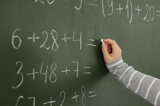 Schoolboy doing math on chalkboard in classroom, closeup