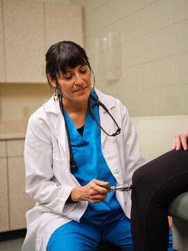 Nurse in scrubs checks woman's reflexes with hammer
