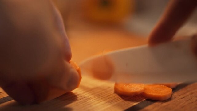 A man's hands meticulously cut vibrant orange carrots on a wooden board, preparing a fresh, vitamin-rich meal with raw, healthy vegetables for a nutritious diet