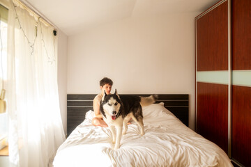 teenage boy lies in bed with his husky dog ​​and looks at his phone, a concept of a leisurely teenage morning routine